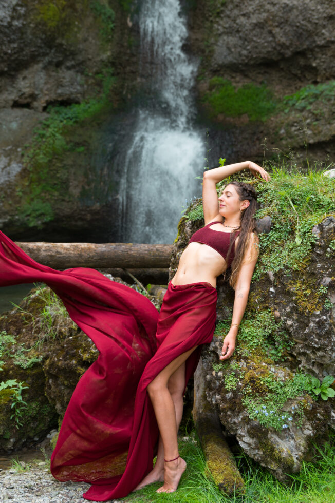 Frau in rotem Kleid vor Wasserfall mit wehendem Rock