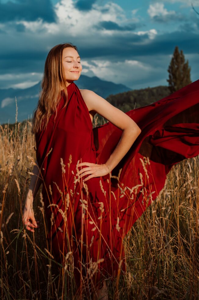 Mama mit rotem Kleid posiert auf offenem Feld bei Sonnenuntergang