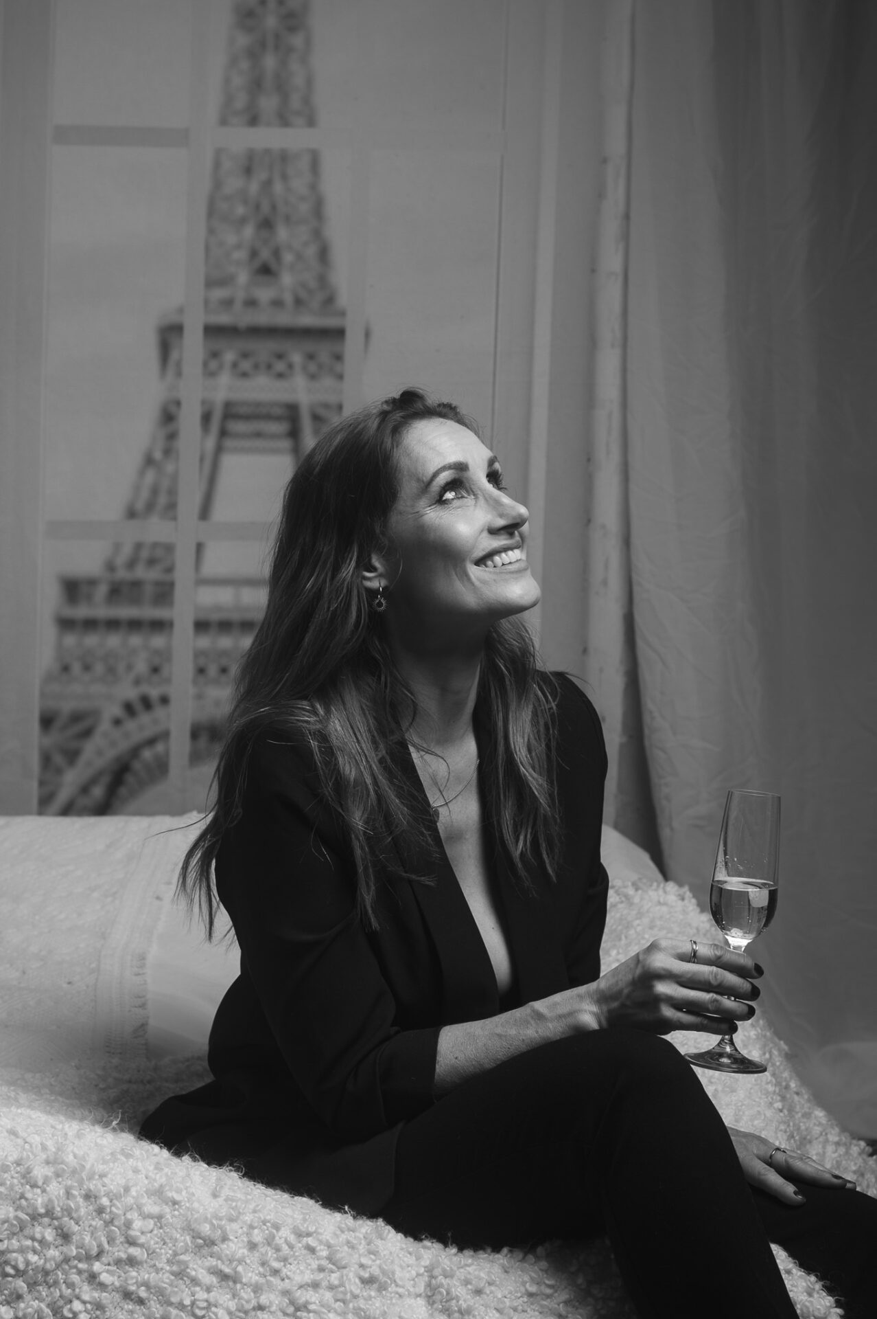 Eine Frau, lachend, mit ein Glas Champagne, Im Hintergrund den Eiffelturm.