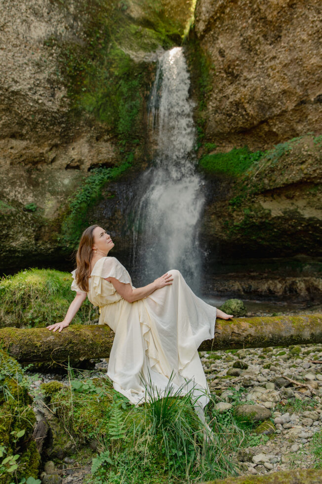 Beeindruckendes bild von ein frau sitzend in ein weisses kleid, auf einen baumstamm vor ein sehr grosse wasserfall.