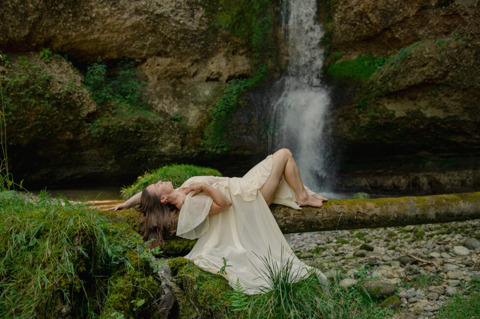 Outdoor boudoir bild, Frau liegt in ein weisses kleid auf einem baumstamm vor grosse Wasserfall