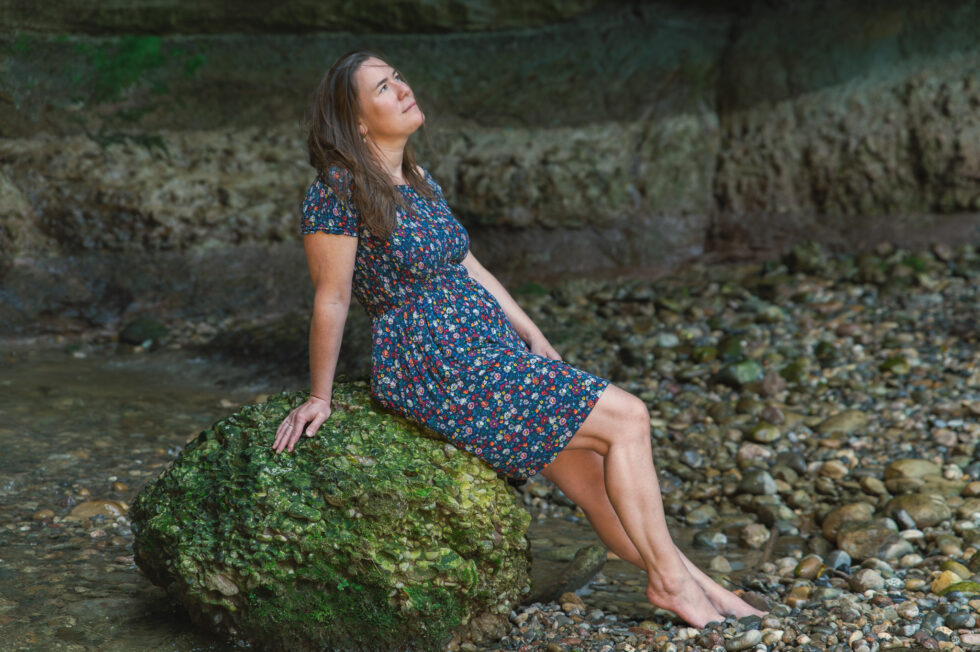 Frau sitzend auf ein grosse stein beim wasserfall